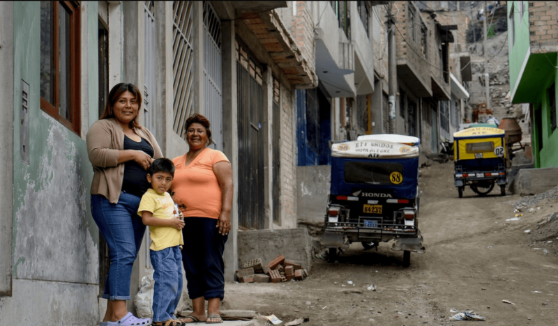 Mother, son, and grandmother pose outside their home, smiling at the camera.