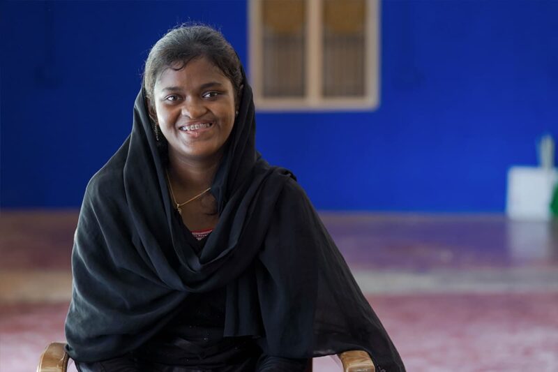 Woman sat in chair smiling at the camera against a blue wall 