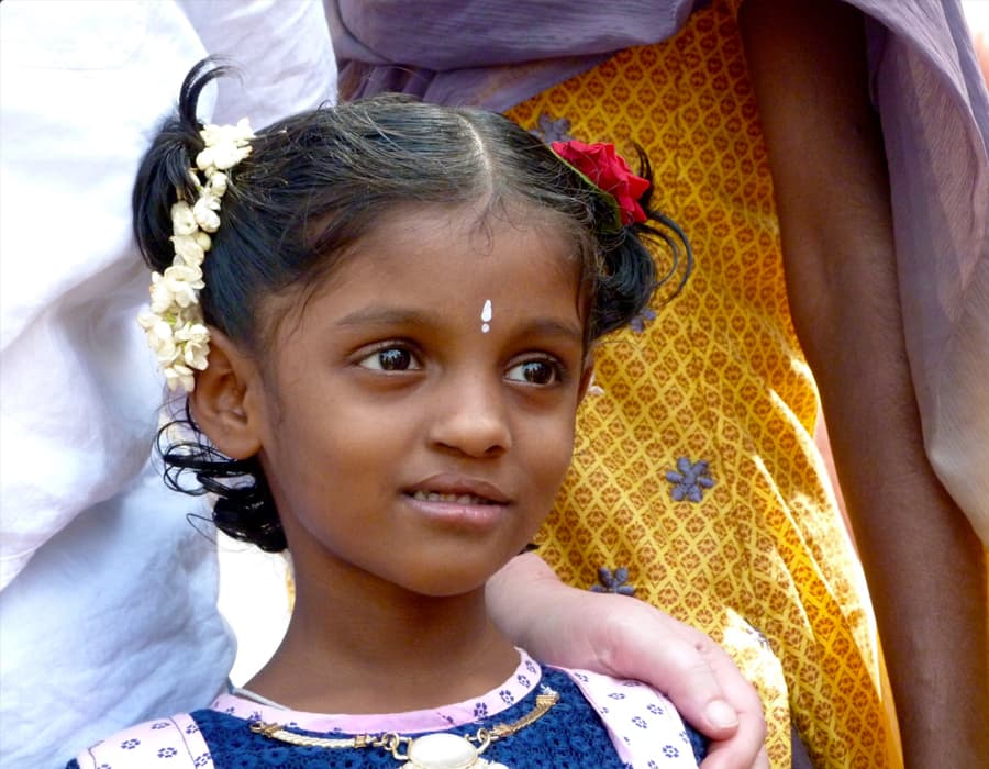 home-tf-difference Close up of child looking outward, with her parents hand on her shoulder.