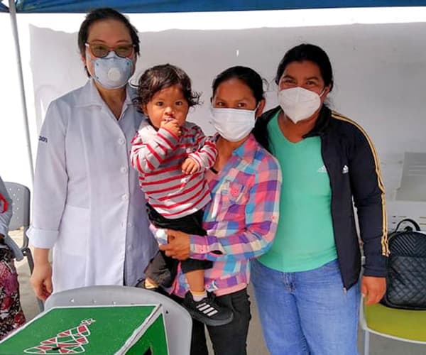 A group of two women and their small boy who as a cleft palate, smiling at the camera with a doctor.